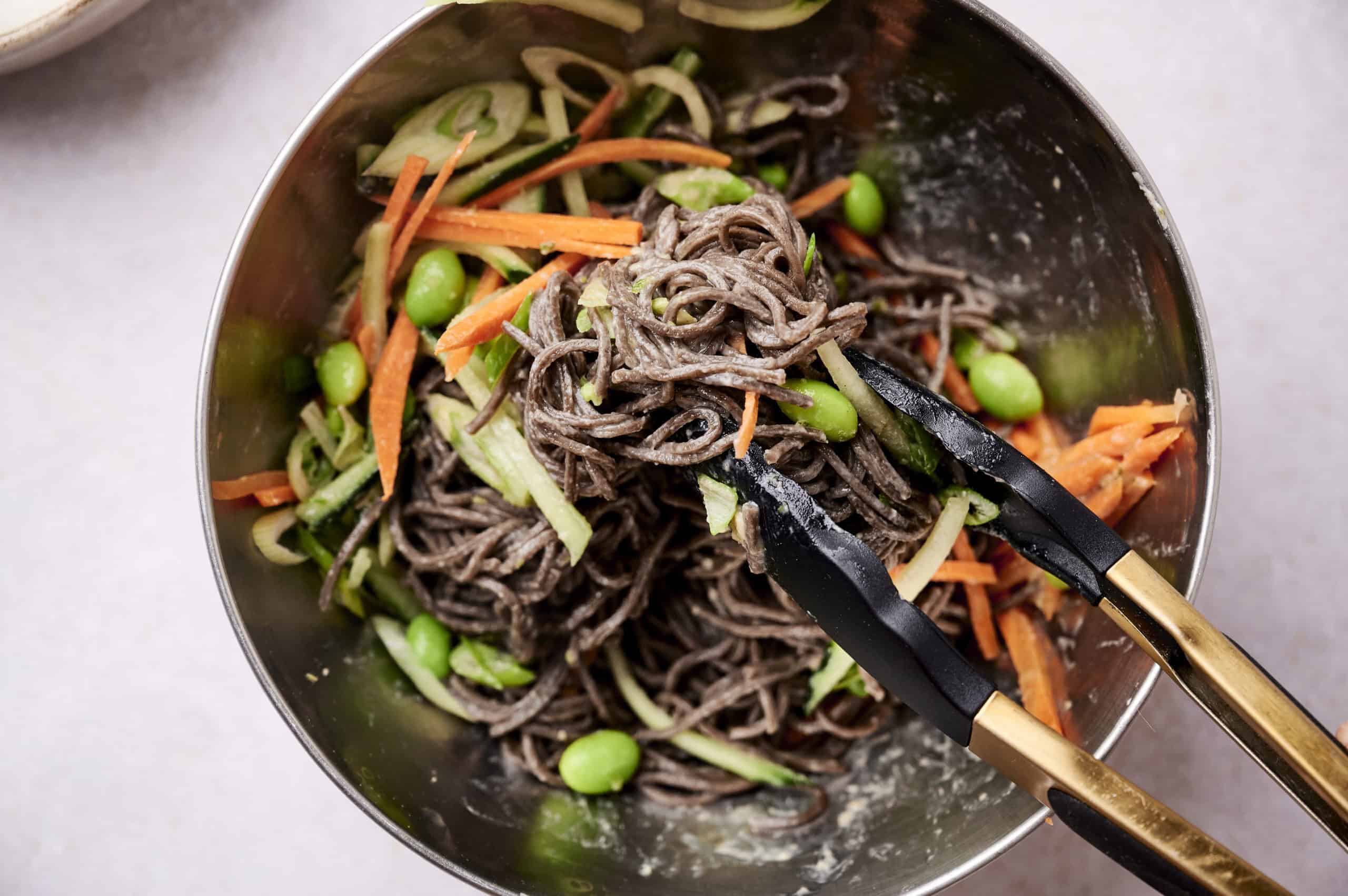 combining noodles, vegetables, and dressing 