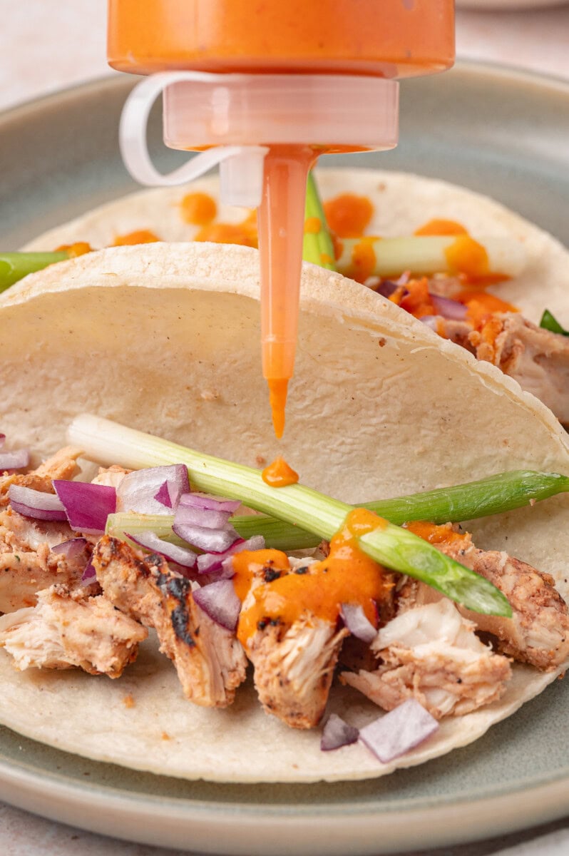 Orange taco sauce being squeeze into tacos 